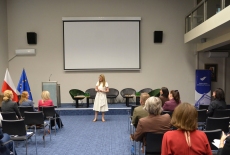 Na środku auli stoi Pani i przemawia przed uczestnikami