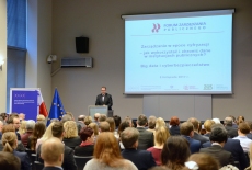 Uczestnicy seminarium w auli KSAP, Dyrektor KSAP przemawia przy mównicy, w tle na dużym ekranie wyświetlona prezentacja z tytułem i logo seminarium