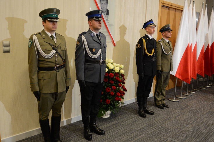 fot. MSWiA Przedstawiciele służb mundurowych pełnią wartę przy tablicy poświęconej śp. Władysławowi Stasiakowi. W tle flagi biało-czerwone.